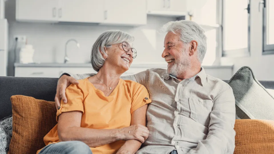 Smiling senior couple sitting together on a sofa at home, sharing a relaxed and happy moment